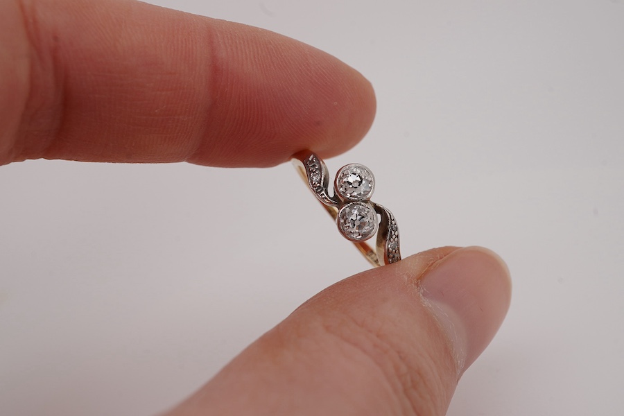 A diamond toi-et-moi ring, early 20th century, collet-set with two circular-cut diamonds totalling approximately 0.30 carats, to sinuous shoulders set with single-cut diamonds, size K, stamped 18ct PLAT, Condition: good